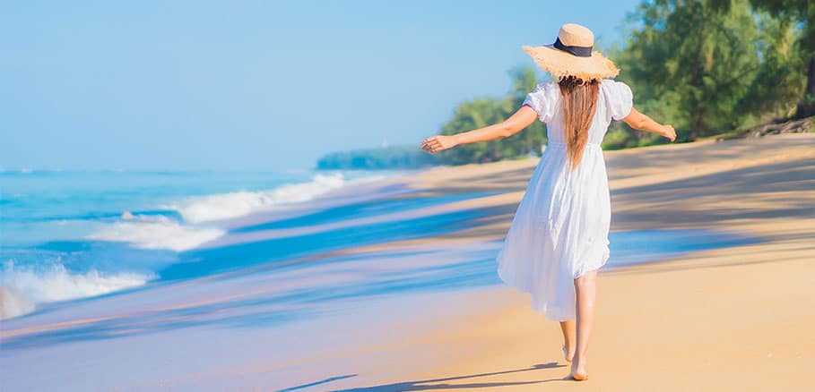 Γυναίκα με λευκό μακρύ παρεό που της παρέχει αντηλιακή προστασία σε παραλία.