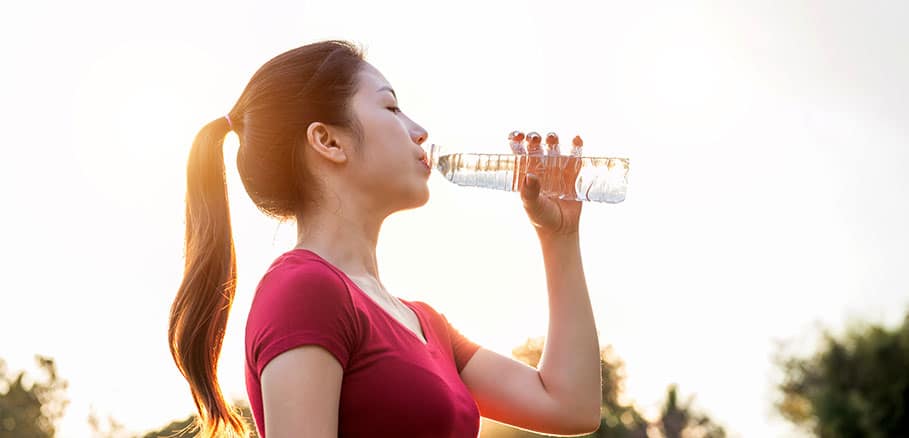Γυναίκα με κόκκινο t-shirt σε εξωτερικό χώρο πίνει νερό από πλαστικό μπουκάλι.